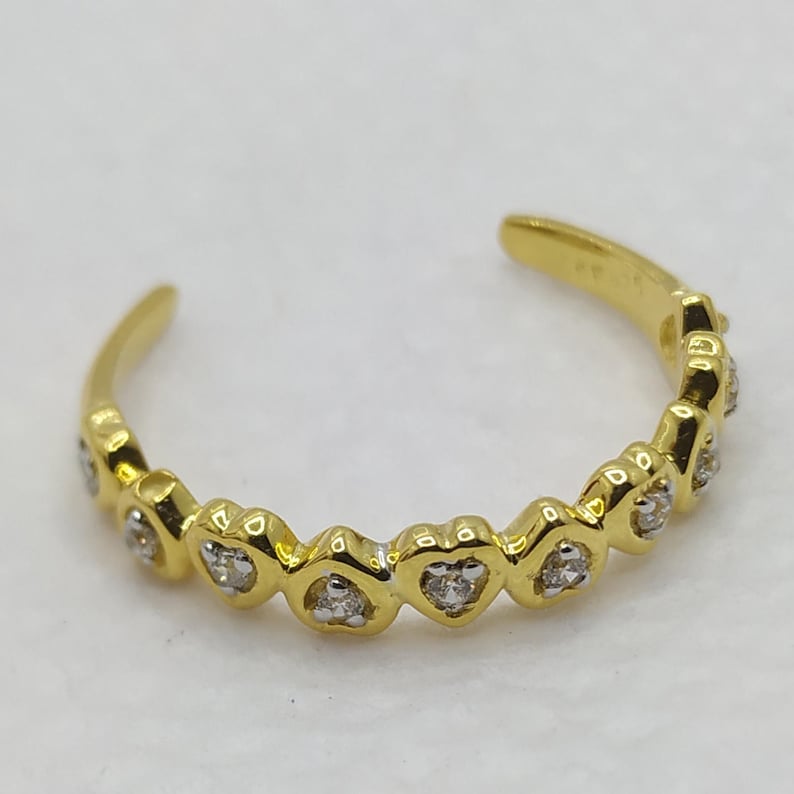 May include: A gold toe ring with a row of small, clear stones set in heart-shaped settings.