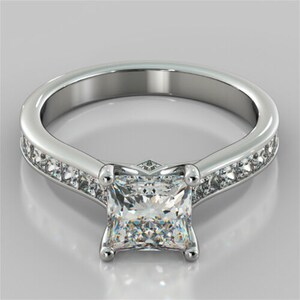 Puede incluir: Un anillo de compromiso de plata con una piedra central de diamante de forma cuadrada y una banda de diamantes más pequeños.
