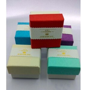 May include: Five small gift boxes in various colors, including red, blue, green, cream, and purple. Each box has a white label with gold lettering that reads "Happiness Just For You" and a small crown icon.