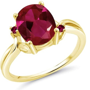 Puede incluir: Un anillo de oro con una gran piedra de rubí ovalada y dos rubíes más pequeños como acentos. El anillo tiene una banda delicada y retorcida.