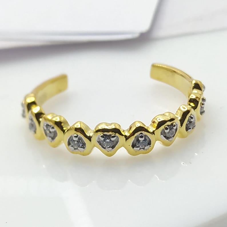 May include: A gold toe ring with a row of small heart-shaped settings, each containing a single clear stone.