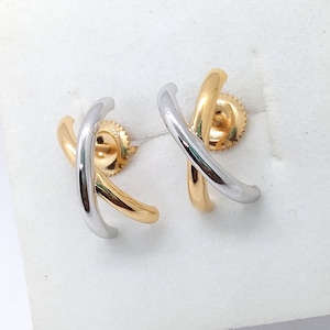 May include: A pair of gold and silver-tone stud earrings. Each earring features an overlapping X design. The posts and backs are gold-colored. The earrings are displayed on a white surface.