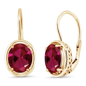 May include: A pair of gold-coloured leverback earrings. Each earring features a large, oval-shaped, deep red gemstone set within a gold bezel. The leverback design is visible, with intricate detailing on the back of the gemstone setting.