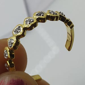 May include: A gold ring with a row of small heart-shaped settings, each with a single clear stone.