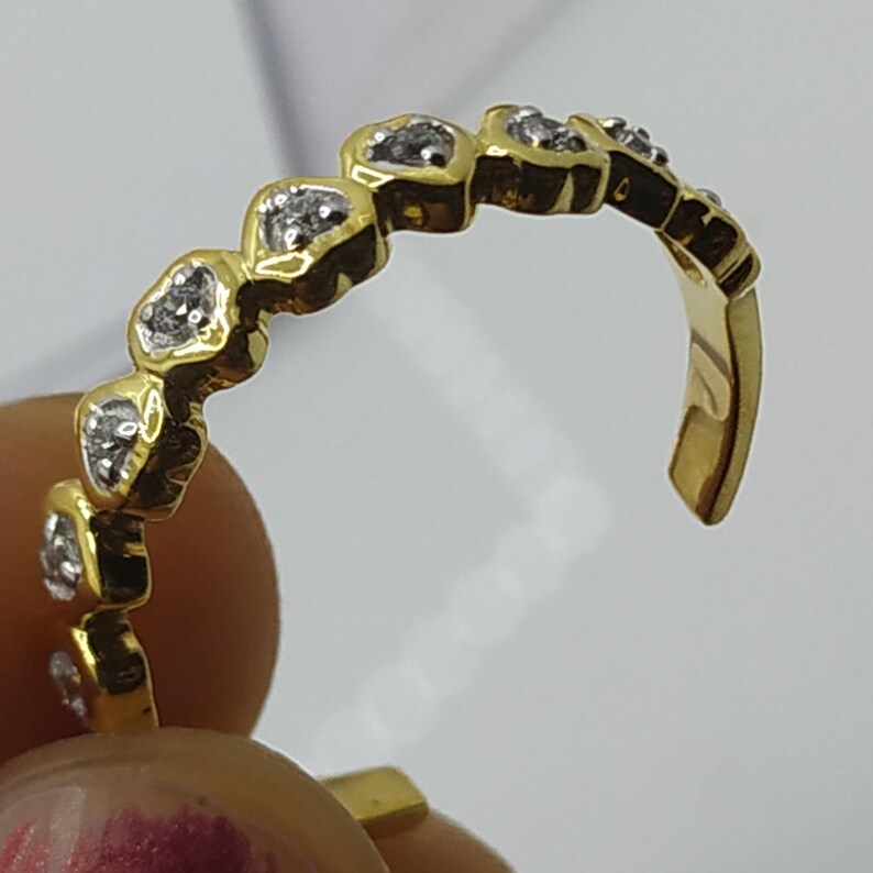 May include: A gold ring with a row of small heart-shaped settings, each with a single clear stone.