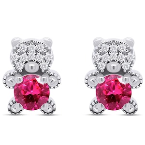 May include: A pair of silver teddy bear stud earrings with a pink gemstone in the centre of each bear. The bears are surrounded by smaller white gemstones.