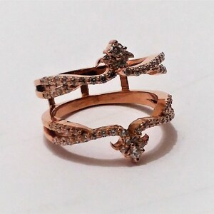 May include: Rose gold double-band ring with sparkling clear stones. The ring features an open design with two bands connected by vertical bars and decorative accents. A unique piece of jewelry.