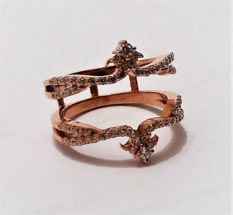 May include: Rose gold double-band ring with sparkling clear stones. The ring features an open design with two bands connected by vertical bars and decorative accents. A unique piece of jewelry.
