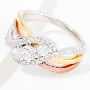 Puede incluir: Un anillo de oro, oro rosa y plata con tres diamantes redondos engastados en pavé. El anillo tiene un diseño de banda trenzada.