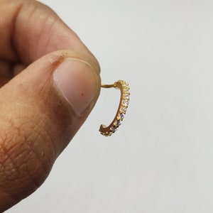 Könnte beinhalten: Ein goldener Nasenring mit einer Reihe kleiner, klarer Steine um den Reifen.