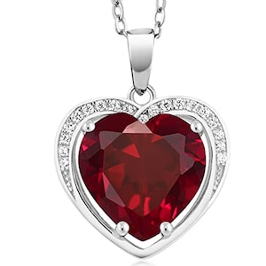May include: A silver heart-shaped pendant necklace with a large red gemstone in the center and a halo of smaller white gemstones around the edge.