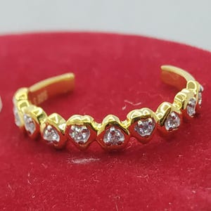May include: A gold toe ring with a row of heart-shaped settings, each containing a small clear stone.