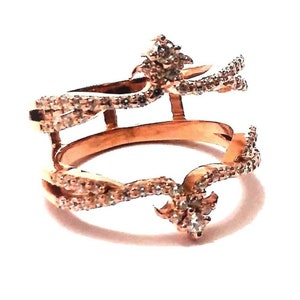 May include: A rose gold ring with a double band design. The ring is set with small, clear stones that create a delicate and intricate pattern.