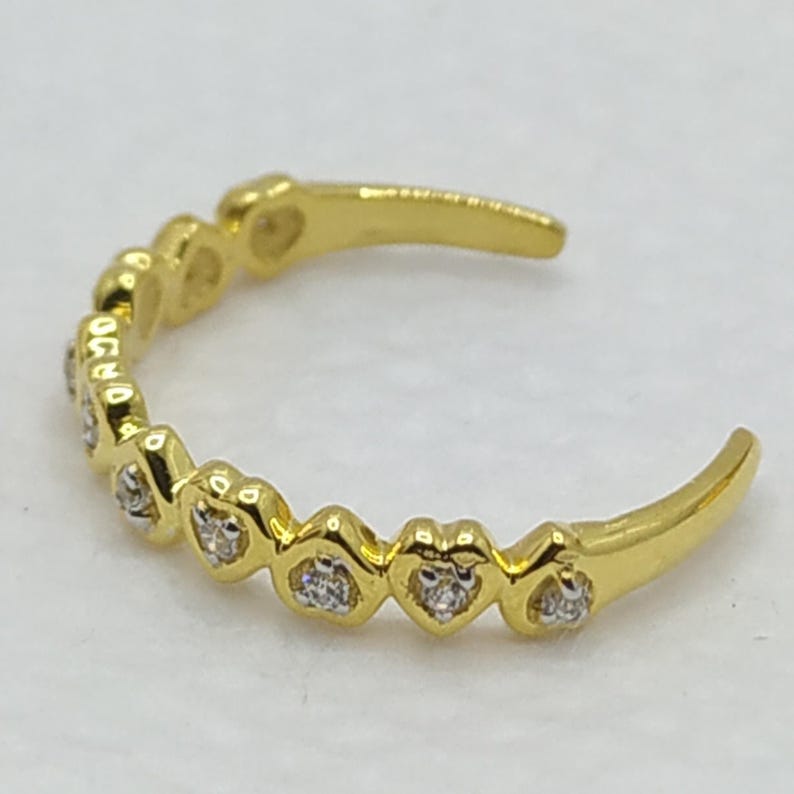 May include: A gold toe ring with a row of small heart-shaped settings, each containing a clear stone.