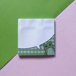 May include: A white notepad with a green and white gingham border. A green frog with a speech bubble is peeking out from the bottom right corner.