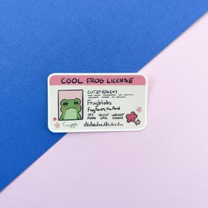 May include: A rectangular sticker with a pink border and the text "COOL FROG LICENSE". The sticker features a cartoon frog with the name "Frogblobs" and the text "Frogtown, the Pond". Additional text includes "SEX", "HEIGHT", "WEIGHT", and "Frogge".