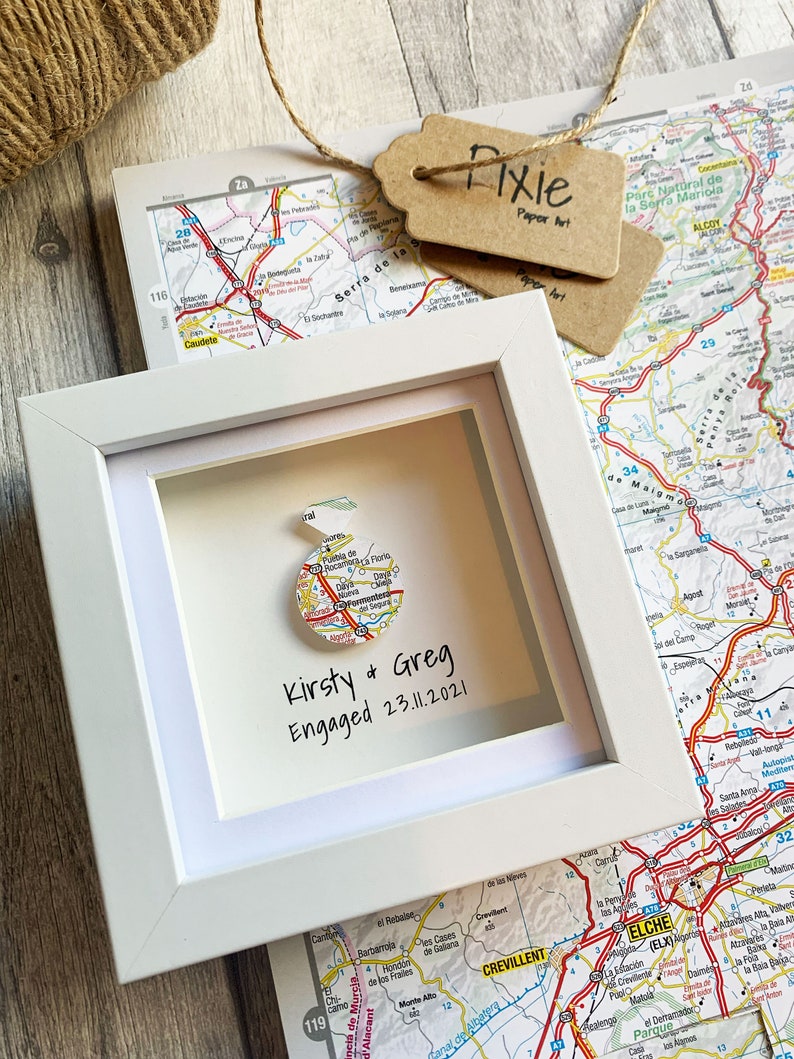 Pu&ograve; includere: Una cornice bianca con una mappa di una citt&agrave; al suo interno. La mappa &egrave; circolare ed &egrave; circondata da un bordo bianco. Il testo "Kirsty & Greg Engaged 23.11.2021" &egrave; scritto sotto la mappa.
