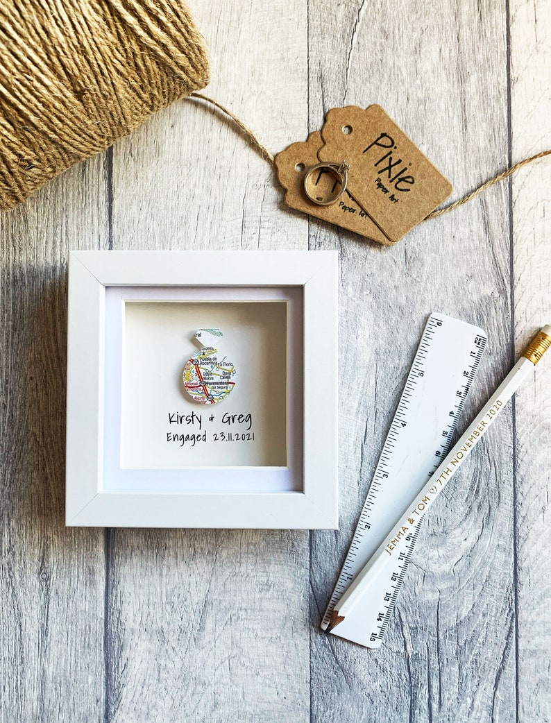 Pu&ograve; includere: Una cornice bianca con una mappa all'interno. La mappa &egrave; un cerchio e ha il testo "Kirsty & Greg Engaged 23.11.2021".