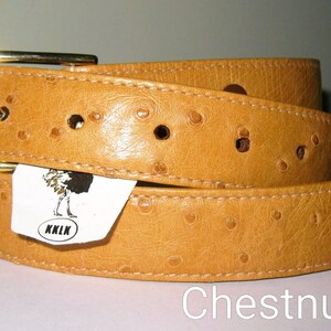May include: A tan belt with a textured ostrich-like pattern and a gold-tone metal buckle. A white tag attached to the belt features a black graphic of an ostrich and the text KKLK. The word Chestnut is printed in white at the bottom right.