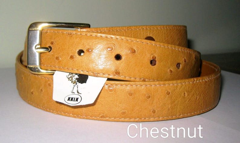 May include: A tan belt with a textured ostrich-like pattern and a gold-tone metal buckle. A white tag attached to the belt features a black graphic of an ostrich and the text KKLK. The word Chestnut is printed in white at the bottom right.
