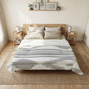 Könnte beinhalten: Ein Bett mit einer weißen Bettdecke mit grauem, von Ikat inspiriertem horizontalem Streifenmuster, vier beigen rechteckigen Kissen und einem hölzernen Kopfteil. Das Bett wird von zwei Nachttischen aus Holz mit Lampen flankiert und steht auf einem Juteteppich.