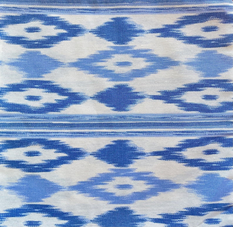 K&ouml;nnte beinhalten: Wei&szlig;er Stoff mit einem blauen und hellblauen geometrischen Muster. Das Muster ist eine sich wiederholende Diamantform mit einer kleineren Diamantform im Inneren.