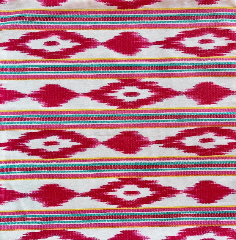 K&ouml;nnte beinhalten: Wei&szlig;er Stoff mit einem sich wiederholenden Muster aus rosa und roten Rauten mit wei&szlig;em Zentrum. Der Stoff hat d&uuml;nne Streifen in Gelb, Rosa und T&uuml;rkis.