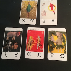 May include: Six tarot cards with astrological symbols. The cards depict various images, including a woman in a green dress, a red figure jumping through a ring, a creature with a long trunk, two figures in flames, a figure with a leafy skirt, and a figure with a leafy skirt.