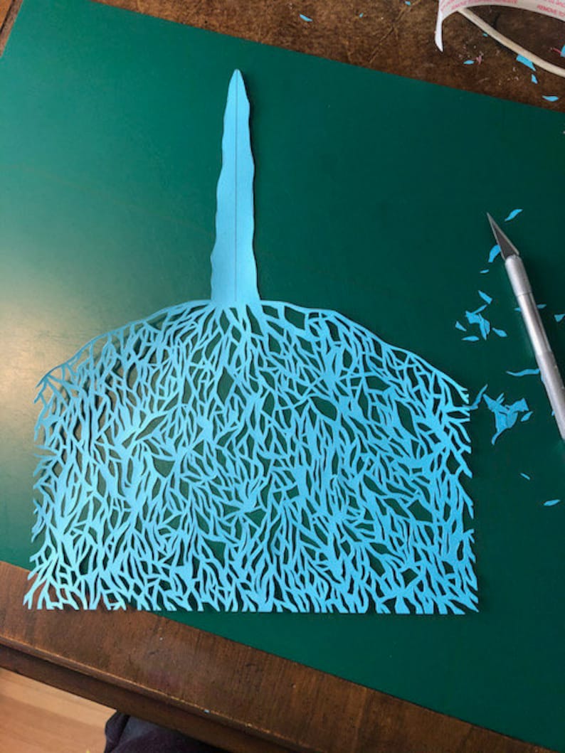 Puede incluir: Un recorte de papel azul de un &aacute;rbol con ramas intrincadas y un solo tronco.