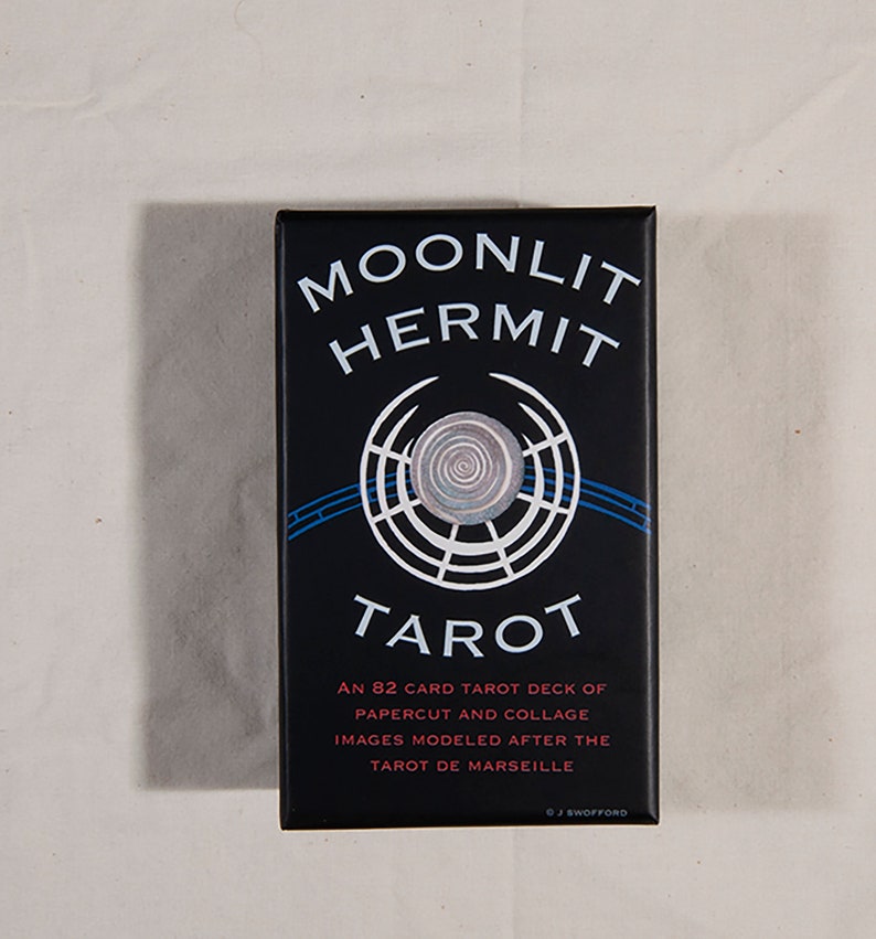 Puede incluir: Una caja negra con el t&iacute;tulo "Moonlit Hermit Tarot" en texto blanco. La caja presenta un dise&ntilde;o circular blanco y azul con una espiral en el centro. El texto "Una baraja de tarot de 82 cartas de recortes de papel y collage de im&aacute;genes modeladas seg&uacute;n el Tarot de Marsella" est&aacute; impreso en blanco en la caja. El s&iacute;mbolo de copyright y "J Swofford" est&aacute;n impresos en blanco en la parte inferior de la caja.