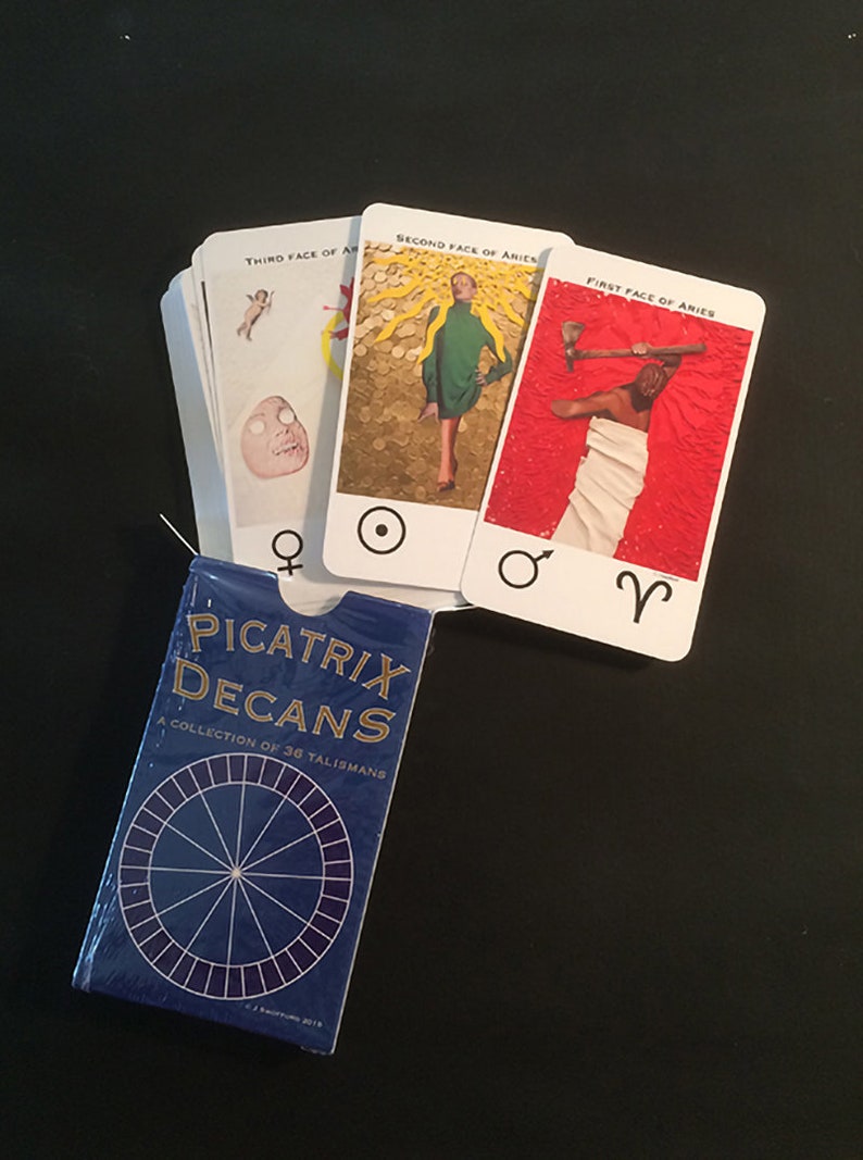 May include: A blue box with the text "Picatrix Decans: A Collection of 36 Talismans" and a circular design. Three cards with images and text are laid out on a black surface.