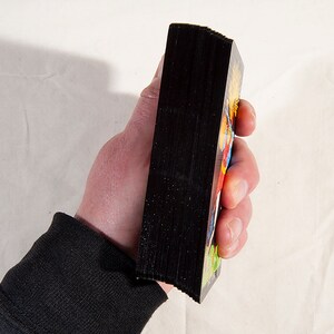 Puede incluir: Una baraja de cartas con el dorso negro y dise&ntilde;os coloridos en el frente. Las cartas est&aacute;n apiladas y se sostienen en una mano.