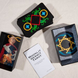 Puede incluir: Una caja negra con una baraja de tarot dentro. La caja tiene un dise&ntilde;o de estrella dorada en la parte superior. La baraja se llama "Moonlit Hermit Tarot".