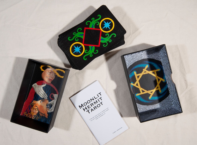 Puede incluir: Una caja negra con una baraja de tarot dentro. La caja tiene un dise&ntilde;o de estrella dorada en la parte superior. La baraja se llama "Moonlit Hermit Tarot".