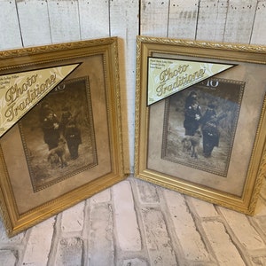 May include: Two gold picture frames with a brown mat and a black and white photo of a family with a dog. The frames have a decorative border and the text "Photo Traditions" is on the front of the frames.