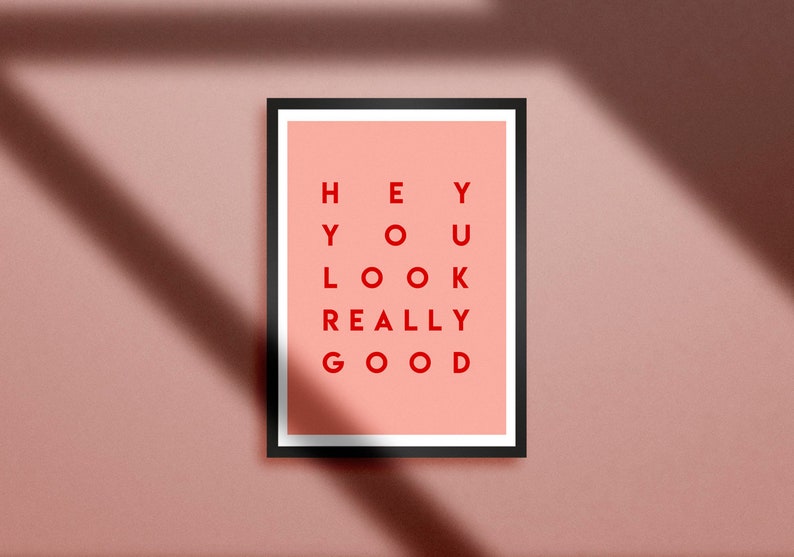 Pu&ograve; includere: Una stampa artistica incorniciata con la scritta "HEY YOU LOOK REALLY GOOD" in lettere rosse su sfondo pesca. La cornice nera &egrave; rettangolare. La stampa &egrave; esposta su una parete rosa con ombre.
