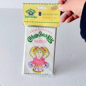 Könnte beinhalten: Eine Packung mit acht Cabbage Patch Kids Party-Einladungen. Die Einladungen zeigen eine Cartoon-Illustration eines Cabbage Patch Kids mit einer Geburtstagstorte. Die Verpackung hat eine gelbe Kopfzeile mit dem Text "8 Einladungen".