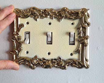 May include: A decorative light switch plate with a gold ornate frame and three white toggle switches.