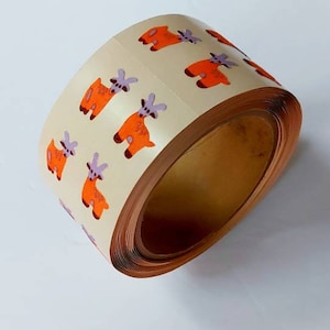 Op de afbeelding: Rol stickers met oranje en paarse cartoon geiten op een crèmekleurige achtergrond.