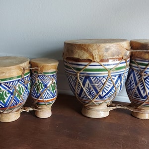 May include: Three ceramic drums with leather tops. The drums are decorated with blue, green, and white geometric patterns. The drums are connected together.