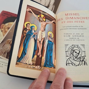 May include: An open book with the title "MISSEL DES DIMANCHES ET DES FETES" in red lettering, featuring a religious illustration of Jesus on the cross. Several religious cards are visible.