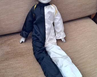 May include: A porcelain doll dressed as a clown. The doll has a white face with black painted features and is wearing a black and white costume with gold trim.