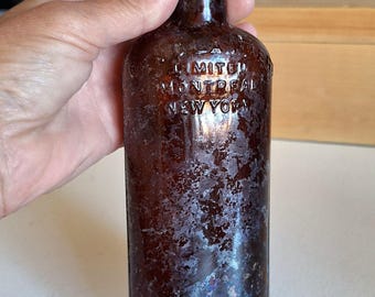May include: A brown glass bottle with a dark cap. The bottle has a cylindrical shape and is covered in a textured, mottled pattern. The text "LIMITED MONTREAL NEW YORK" is embossed on the bottle.