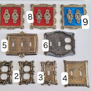 May include: A collection of decorative light switch covers in various styles. Includes ornate, vintage-style covers in gold, bronze, red, and blue. Some have double switch openings, while others have single or outlet configurations. The covers are made of metal.