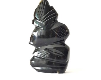 May include: A black obsidian sculpture of a stylized human figure with a headdress. The sculpture is carved with intricate details and has a smooth, polished finish.
