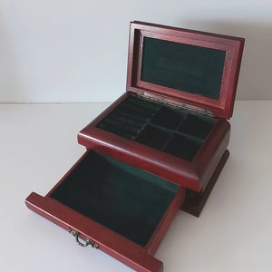May include: A wooden jewellery box with a hinged lid and a pull-out drawer. The box is lined with green felt and has compartments for storing rings and other small items.