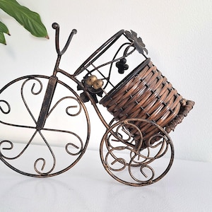 Peut inclure: Porte-bouteille de vin décoratif en forme de bicyclette. Le cadre en métal de couleur bronze supporte un panier tressé pour la bouteille. La bicyclette présente des volutes décoratives sur les roues et un détail de grappe de raisin.