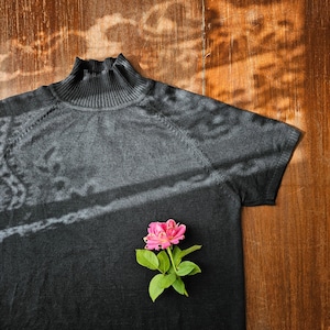 May include: A black mock neck shirt with short sleeves and a pink flower on the front.