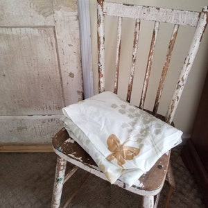 May include: A white wooden chair with a distressed finish, a white and brown patterned fabric is folded and placed on the seat of the chair.