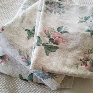 May include: A stack of three white cotton pillowcases with a floral pattern featuring pink and green flowers. The floral pattern is a delicate design with a paisley-like background.